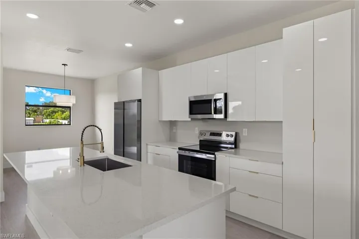 Kitchen featuring hanging light fixtures, light wood-type flooring, appliances with stainless steel finishes, sink, and a center island with sink