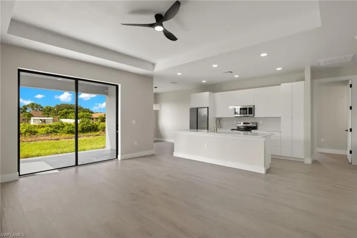 Unfurnished living room with light hardwood / wood-style flooring, ceiling fan, sink, and a tray ceiling