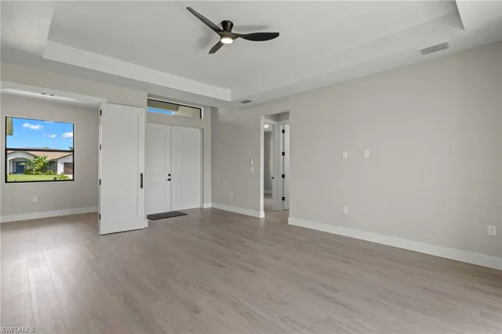 Unfurnished bedroom featuring a tray ceiling, light wood-type flooring, and ceiling fan