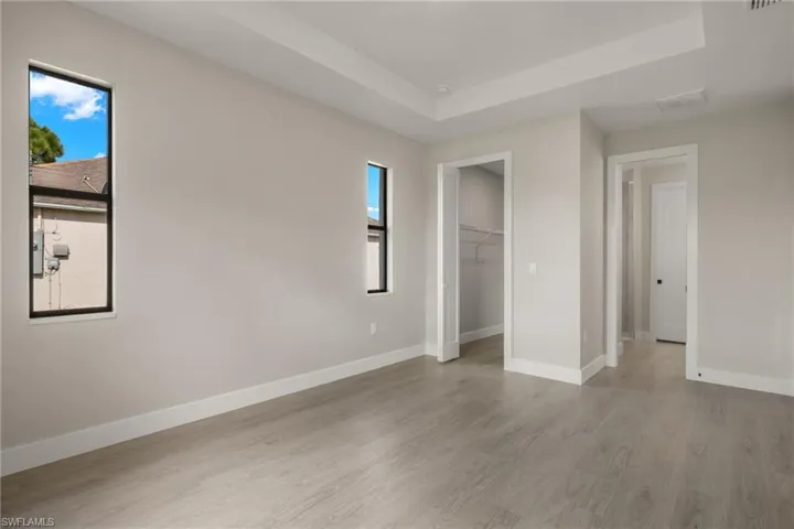 Unfurnished bedroom featuring light wood-type flooring, multiple windows, a tray ceiling, and a closet