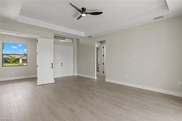 Unfurnished bedroom featuring a tray ceiling, light wood-type flooring, and ceiling fan