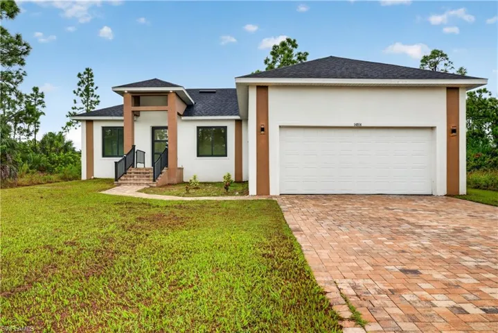 Modern single-story exterior featuring a paver driveway, neutral stucco facade with contrasting vertical accents, asphalt shingle roof, and a raised entryway with metal handrails