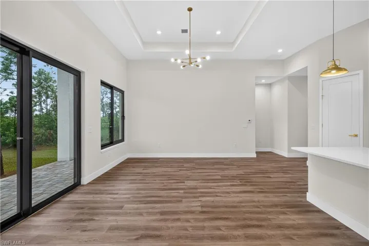 Tray ceiling with recessed lighting, multi-arm metal chandelier, wood-finish flooring, sliding glass door with black frame, and pendant lighting