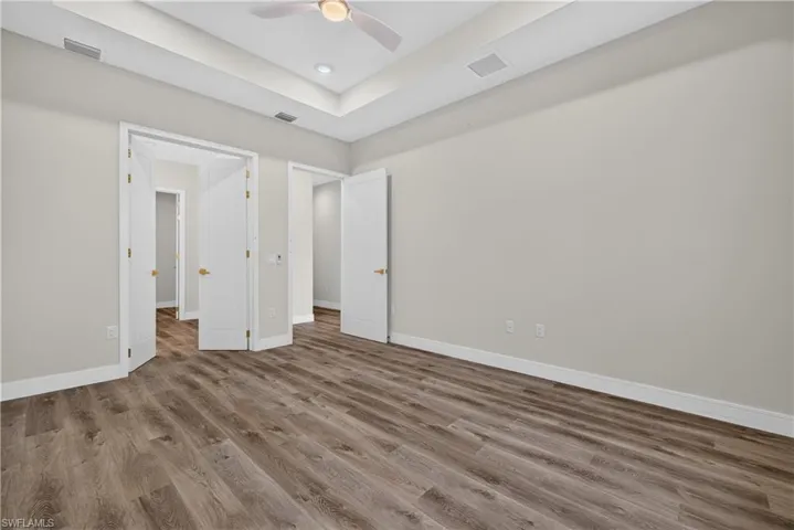 Tray ceiling with a central white ceiling fan, recessed lighting, wood-finish flooring, and multi-panel interior doors with brass-tone hardware