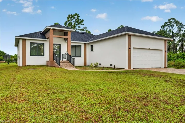 Contemporary exterior featuring a stucco facade, brick accent columns, asphalt shingle roof, paved driveway, and metal railing at the entryway