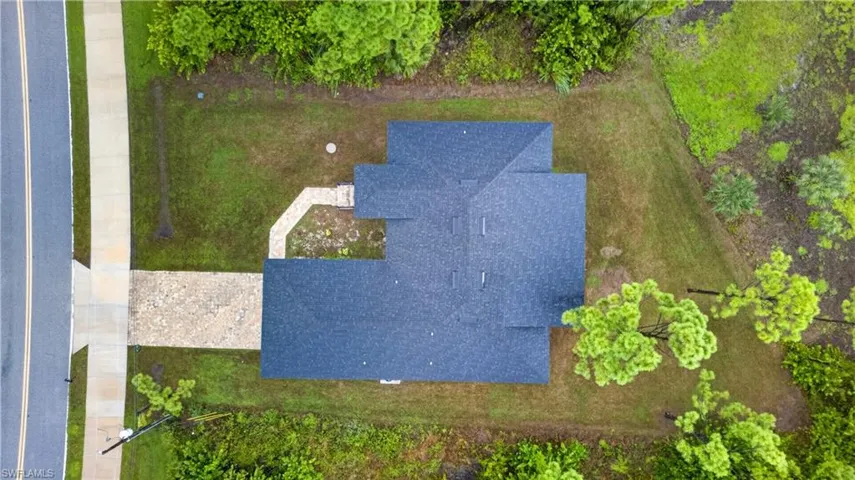 Aerial perspective featuring a multi-gabled shingle roof, stone-paved driveway, and stone walkway situated on a lot with perimeter vegetation