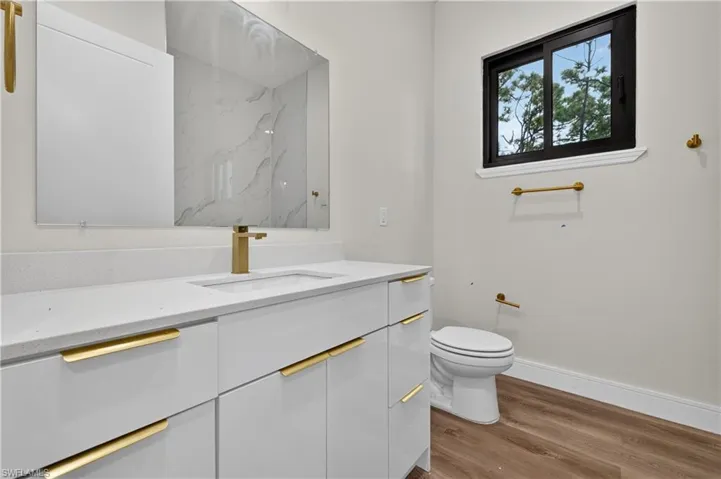 Glossy white vanity with stone-style countertop, integrated undermount sink, brass hardware, and large frameless mirror with stone-style backsplash