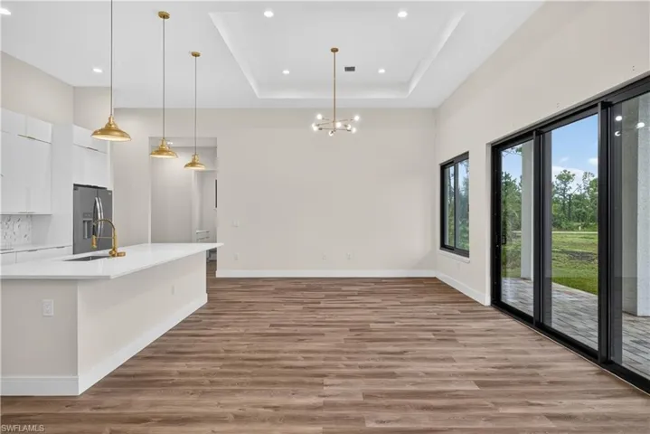 Open-concept interior featuring wood-finish flooring, a kitchen island with quartz countertops, a tray ceiling with recessed lighting, brass-finish pendant lighting, and multi-panel sliding glass doors