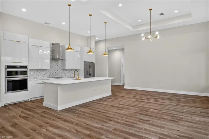 Kitchen featuring high-gloss white cabinetry, center island with quartz countertop, wood-finish flooring, tray ceiling, and brass-tone pendant lighting
