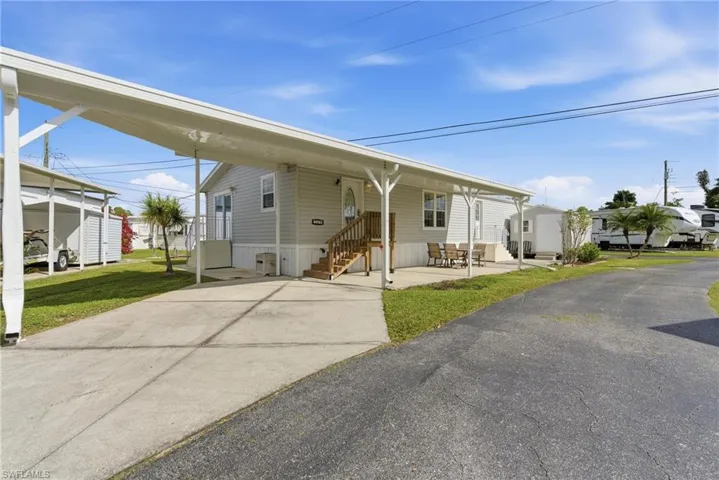 View of front facade with an attached carport, driveway, entry steps, and a front lawn