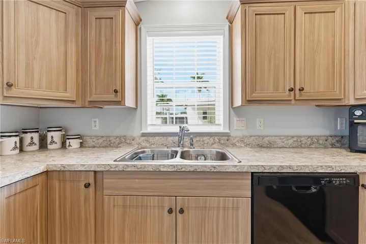 Kitchen with black dishwasher, light countertops, and light brown cabinets