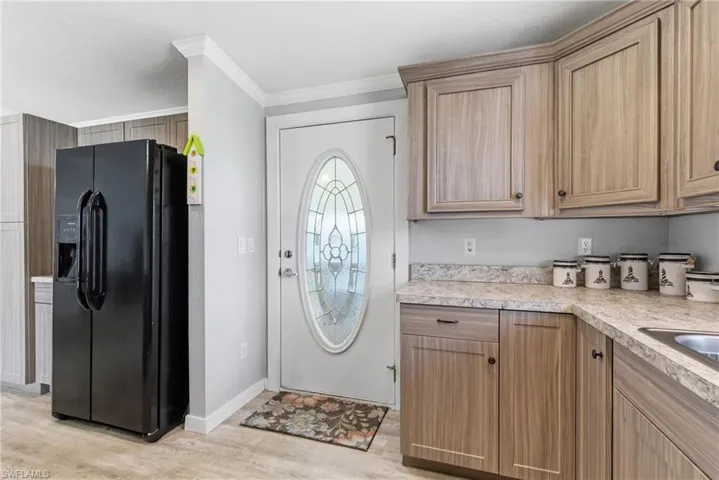 Kitchen featuring black refrigerator with ice dispenser, light countertops, light wood-style flooring, and ornamental molding