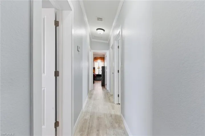 Hall with light wood-style floors, a textured wall, and crown molding