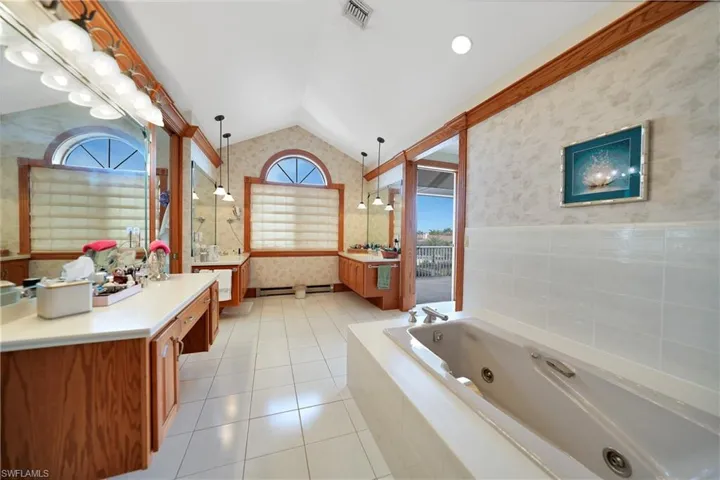 Bathroom with vanity, vaulted ceiling, tile patterned floors, and a relaxing tiled tub