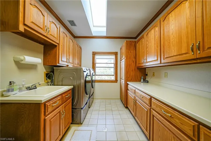 Washroom featuring cabinets, light tile patterned floors, sink, a skylight, and washing machine and dryer
