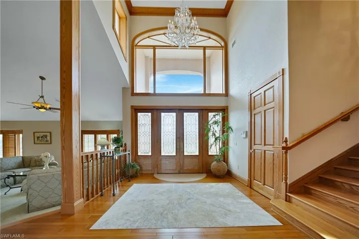 Entrance foyer featuring light wood-type flooring, ceiling fan with notable chandelier, ornamental molding, and a towering ceiling