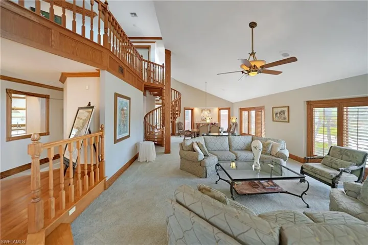 Living room with lofted ceiling, ceiling fan with notable chandelier, and light carpet
