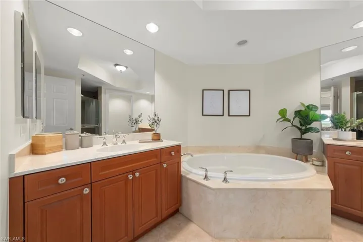Bathroom featuring a stall shower, two vanities, a bath, and recessed lighting