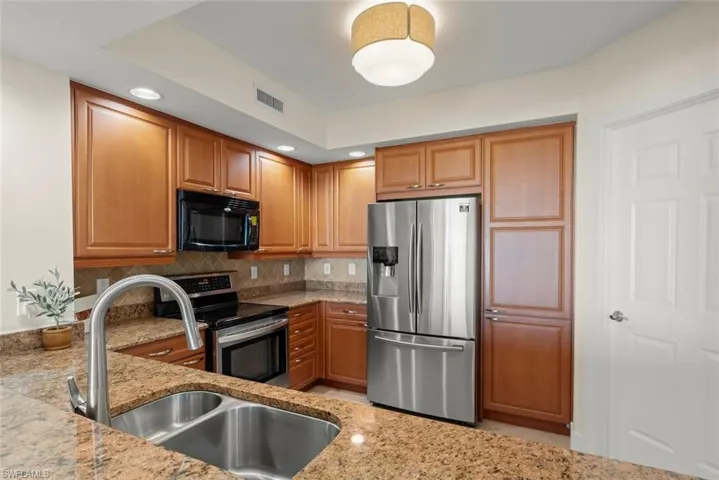 Kitchen with stainless steel appliances, brown cabinetry, light stone counters, backsplash, and recessed lighting