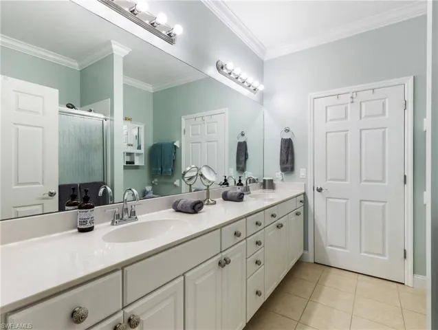 Bathroom with double vanity, crown molding, a stall shower, and light tile patterned floors