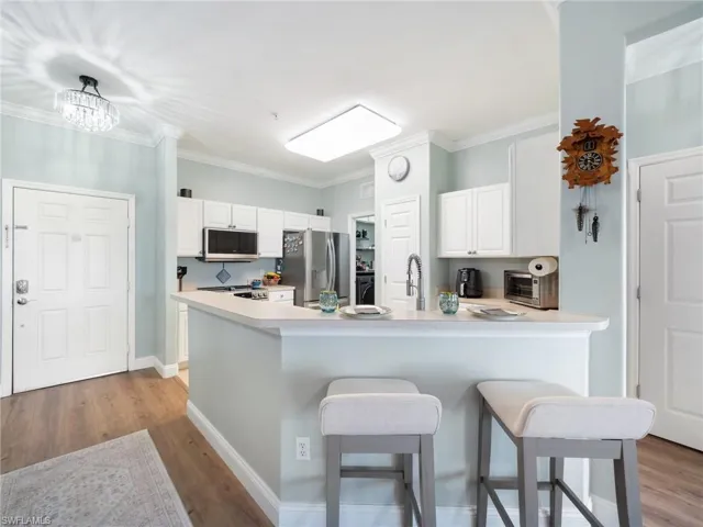 Kitchen featuring a breakfast bar, white cabinetry, light wood-type flooring, light countertops, and ornamental molding