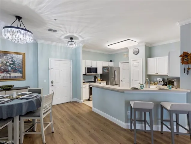Kitchen featuring white cabinets, a breakfast bar area, light wood-type flooring, stainless steel appliances, and crown molding