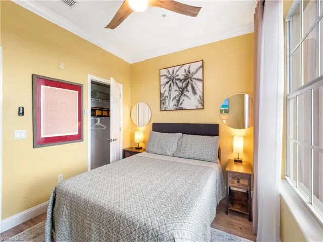 Bedroom with wood finished floors, ornamental molding, ceiling fan, and a spacious closet