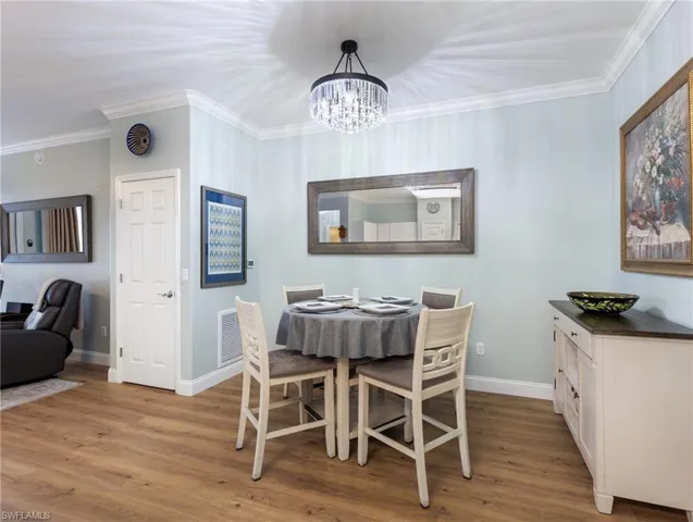 Dining room with light wood-style floors, ornamental molding, and suspended lighting