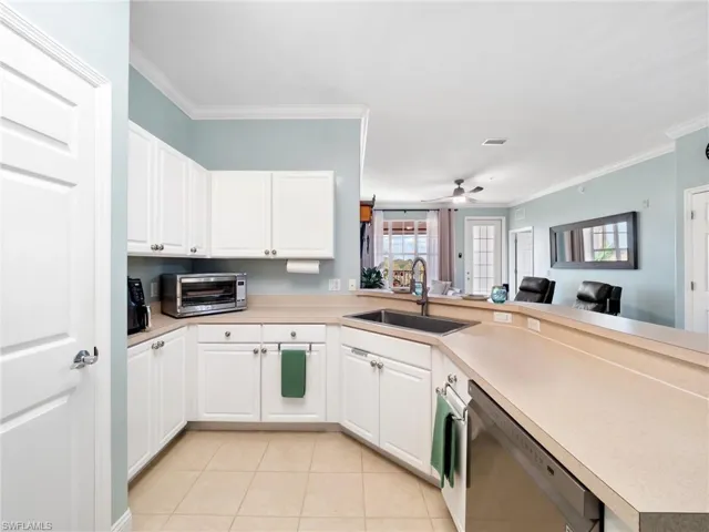 Kitchen featuring open floor plan, stainless steel dishwasher, white cabinets, light countertops, and crown molding