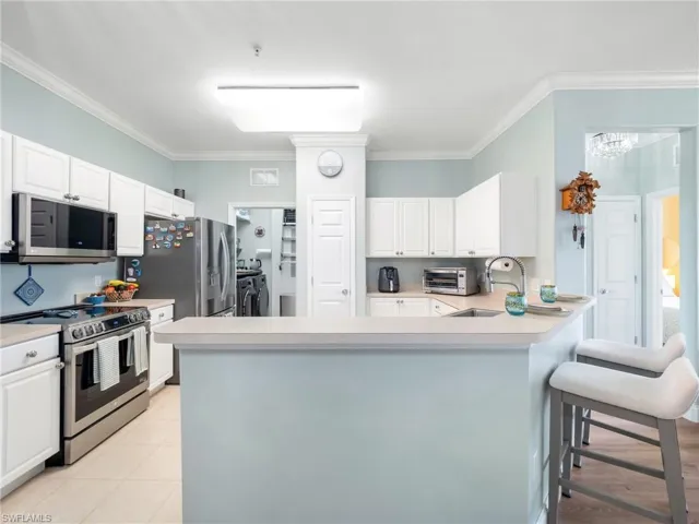 Kitchen with stainless steel appliances, light countertops, white cabinets, crown molding, and a peninsula