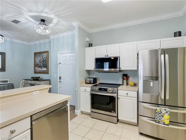 Kitchen featuring stainless steel appliances, crown molding, light countertops, white cabinetry, and light tile patterned floors