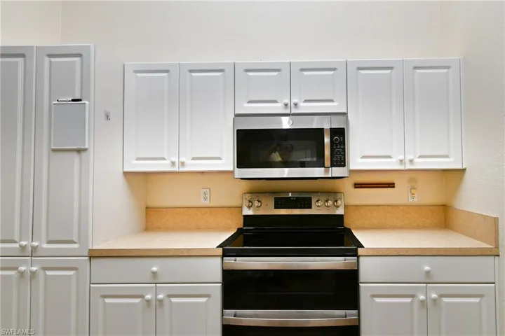 White cabinetry with shaker-style doors, stainless steel microwave, black electric range with a double oven, and solid surface countertops