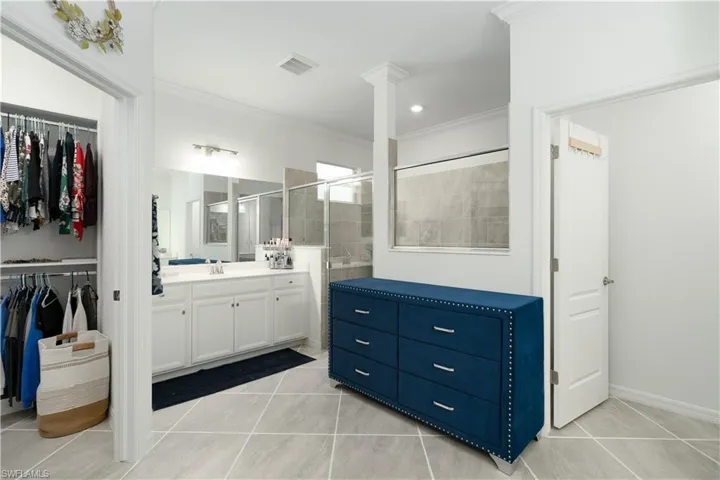 Master Bathroom with dual vanities, tile floors, crown molding, a shower with shower door, large tile shower