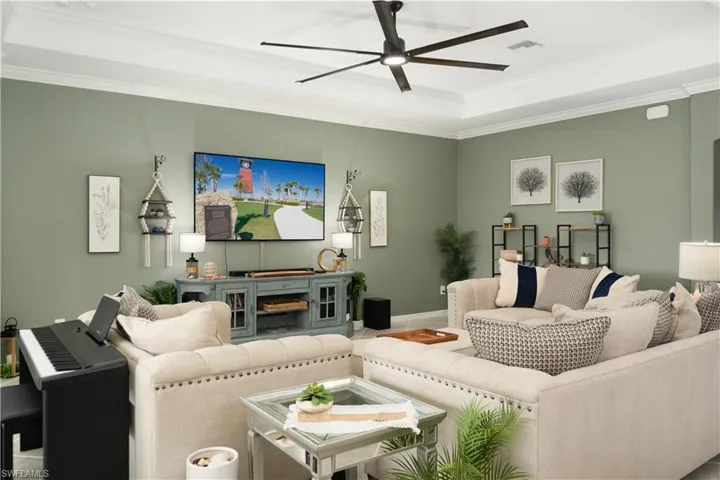 Living room with a tray ceiling, crown molding, and large decorator style ceiling fan. Custom SW Emerld Paint that protects again mold and mildew.