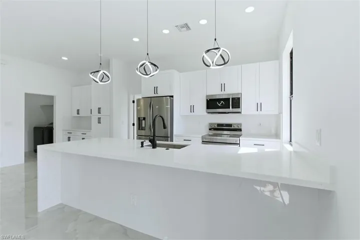 Kitchen with a peninsula, light stone countertops, stainless steel appliances, white cabinetry, and pendant lighting