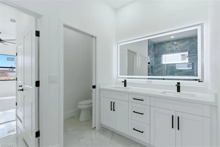 Full bath featuring double vanity, a marble finish shower, ceiling fan, and light marble finish floors