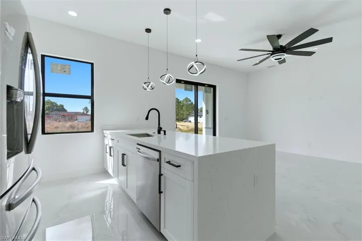 Kitchen with stainless steel appliances, white cabinets, light stone counters, decorative light fixtures, and light marble finish floors