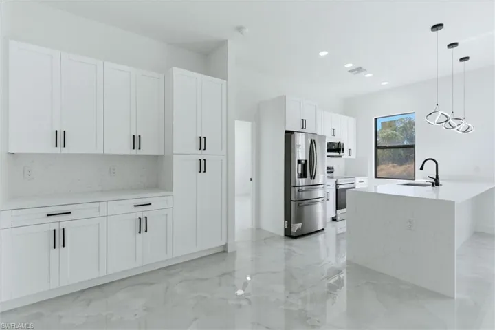 Kitchen with stainless steel appliances, light stone counters, decorative light fixtures, white cabinets, and light marble finish floors