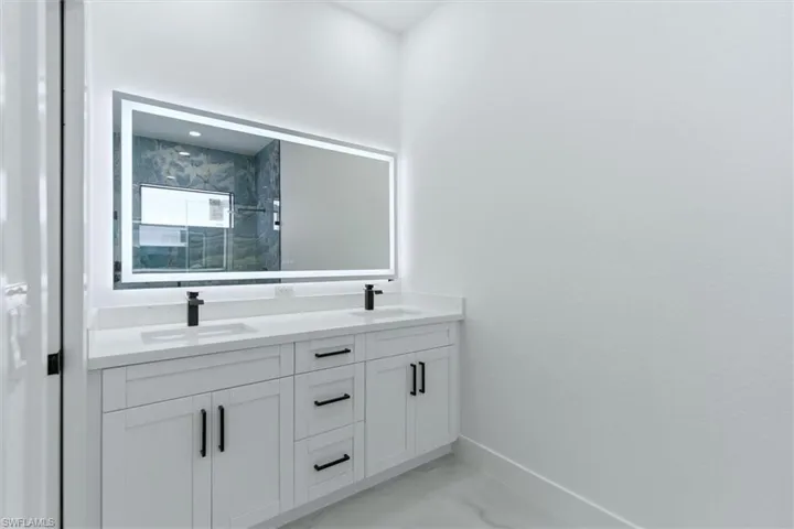 Bathroom featuring double vanity, a marble finish shower, and light marble finish floors