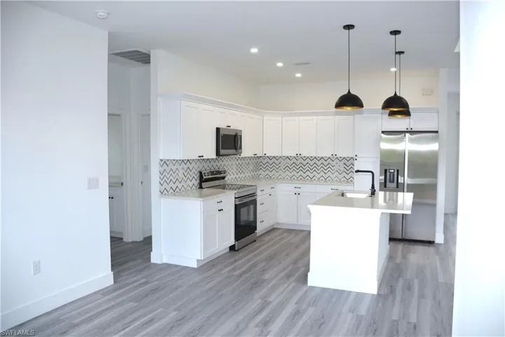Kitchen with tasteful backsplash, sink, White Wood Cabinets, and appliances with stainless steel finishes