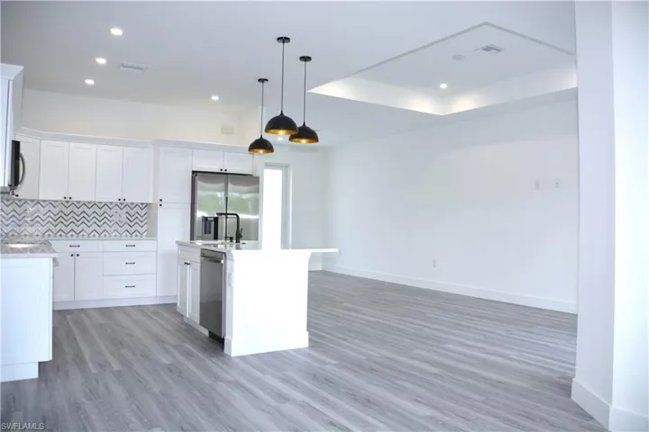 Kitchen featuring decorative light fixtures, backsplash, a kitchen island with sink, white cabinetry, and appliances with stainless steel finishes