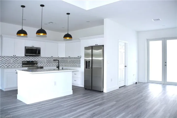 Kitchen with appliances with stainless steel finishes, white cabinets, a kitchen island with sink, backsplash, and water  prove laminated floor