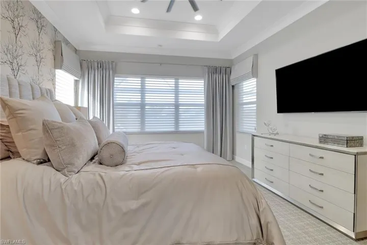 Bedroom featuring ceiling fan, light colored carpet, ornamental molding, and a tray ceiling