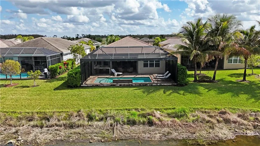 Back of property featuring a water view, glass enclosure, and a lawn