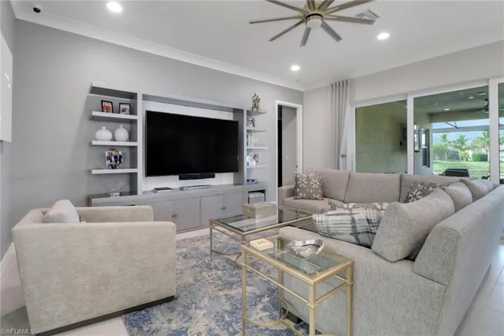 Tiled living room with built in shelves, ornamental molding, and ceiling fan