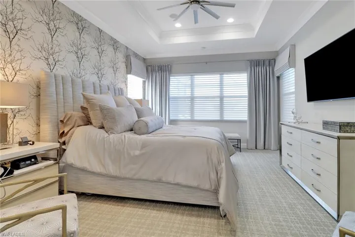 Bedroom with crown molding, light colored carpet, ceiling fan, and a tray ceiling
