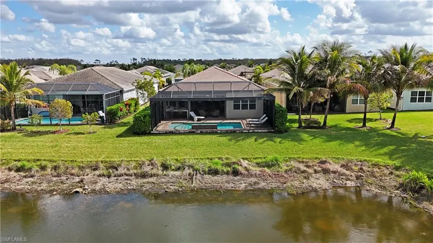 Rear view of house featuring a water view, glass enclosure, and a lawn