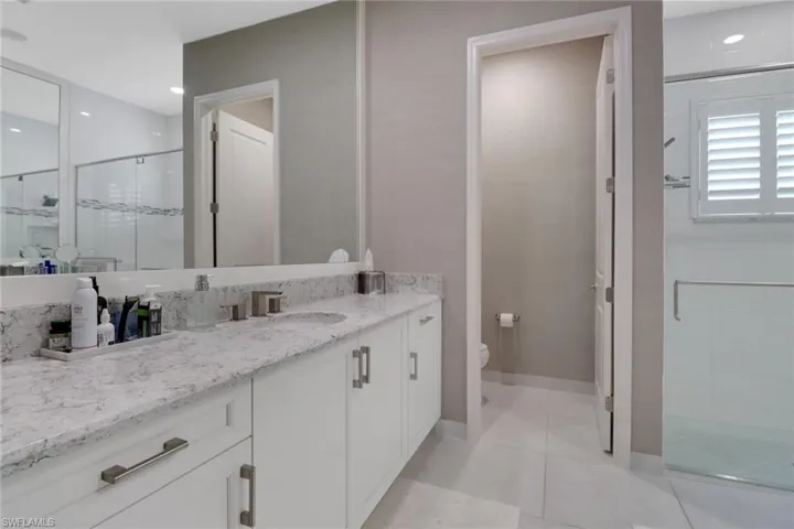 Bathroom with a shower with door, vanity, tile patterned floors, and toilet
