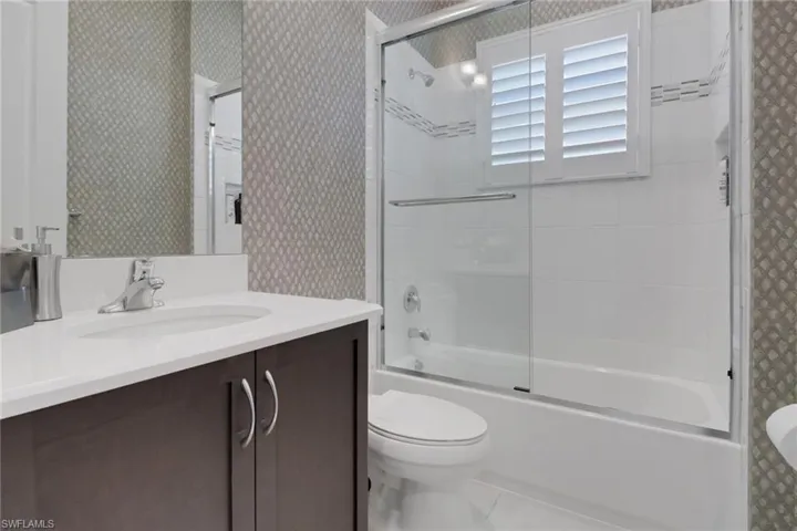 Full bathroom with tile patterned flooring, bath / shower combo with glass door, vanity, and toilet