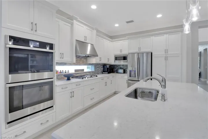 Kitchen featuring stainless steel appliances, white cabinetry, sink, and light stone counters
